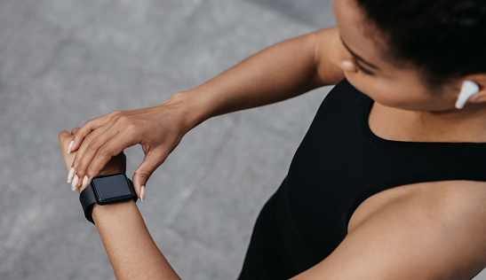 Running and heart rate. Young african american woman checks fitness tracker on arm, jogging with wireless headphones, outdoors, cropped, free space