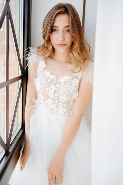 istock beautiful bride in white dress sits by window. 1262894628
