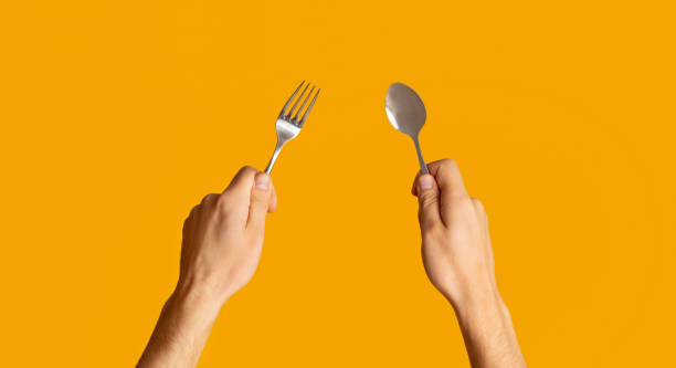 istock Millennial guy showing metal fork and spoon on orange background, closeup 1262894742