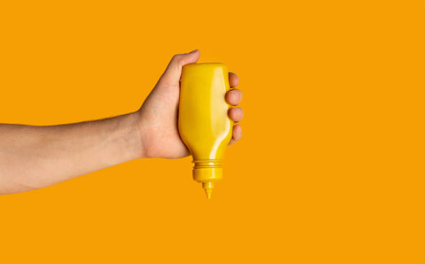 istock Male hand squeezing bottle with mustard on orange background, closeup. Space for text 1262895065