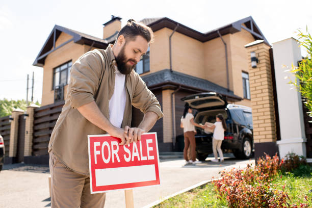 Putting house up for sale Young bearded father placing For sale sign into ground near house while putting house up for sale house for sale by owner stock pictures, royalty-free photos & images