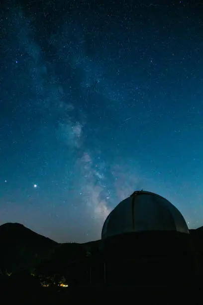 An observatory at night with the milky way in the background. Silhouette of the dome and the mountains.