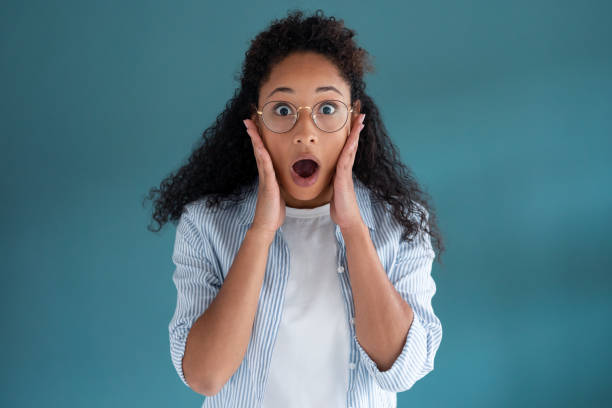 istock Pretty young african american woman looking at camera with surprised expression over blue background. 1262911026