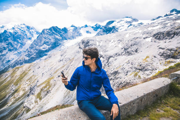 istock Young man using smart phone with view of Stelvio Pass in Italy 1262911148