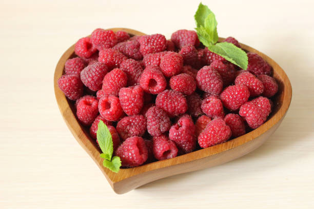 istock Garden raspberries in a wooden container decorated with a mint leaf on a white background 1262911595