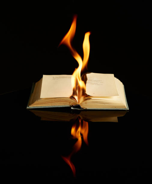 istock Burning book isolated on black background and reflective surface. Concept photography about literature, art, anti-utopia 1262913439