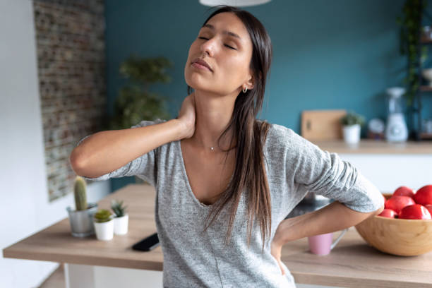 joven cansada que sufre dolor de cuello mientras está sentada en el taburete de la cocina en casa. - backache chiropractic adjustment pain women fotografías e imágenes de stock