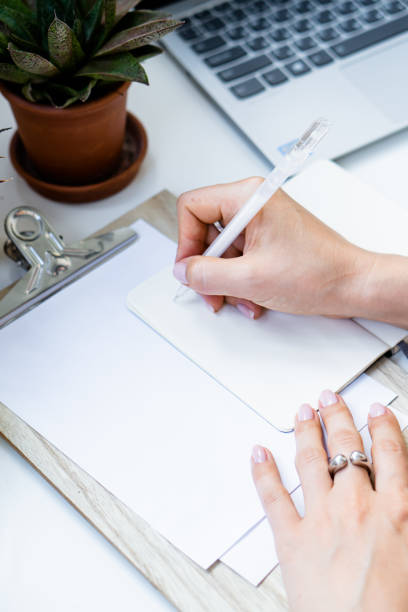 istock Woman's hands making notes in notepad in cozy summer office with laptop and green home plants 1262941617