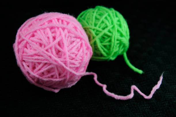 Green and pink wool yarn ball on black background