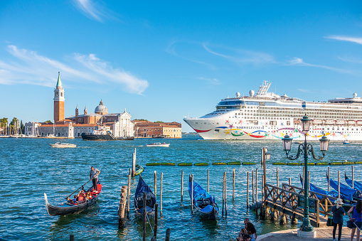 Venice, Italy – August 13, 2017:  Gondola full of people with San Giorgio Maggiore island on the background and an ocean cruiser