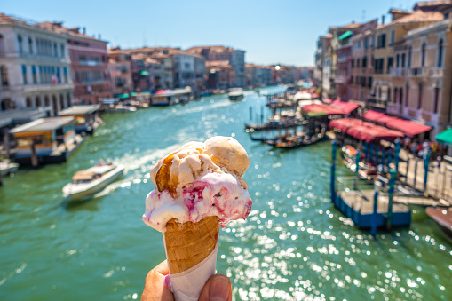 Beautiful and delicious italian gelato in waffle cone in front of streets and bridges of Venice