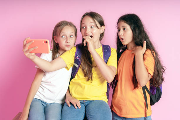 Three teen girls smiling and shoots a video on a pink background.  Selfies. Tiktok blogger. Three teen girls smiling and shoots a video on a pink background.  Selfies. Tiktok blogger. 12 13 years photos stock pictures, royalty-free photos & images