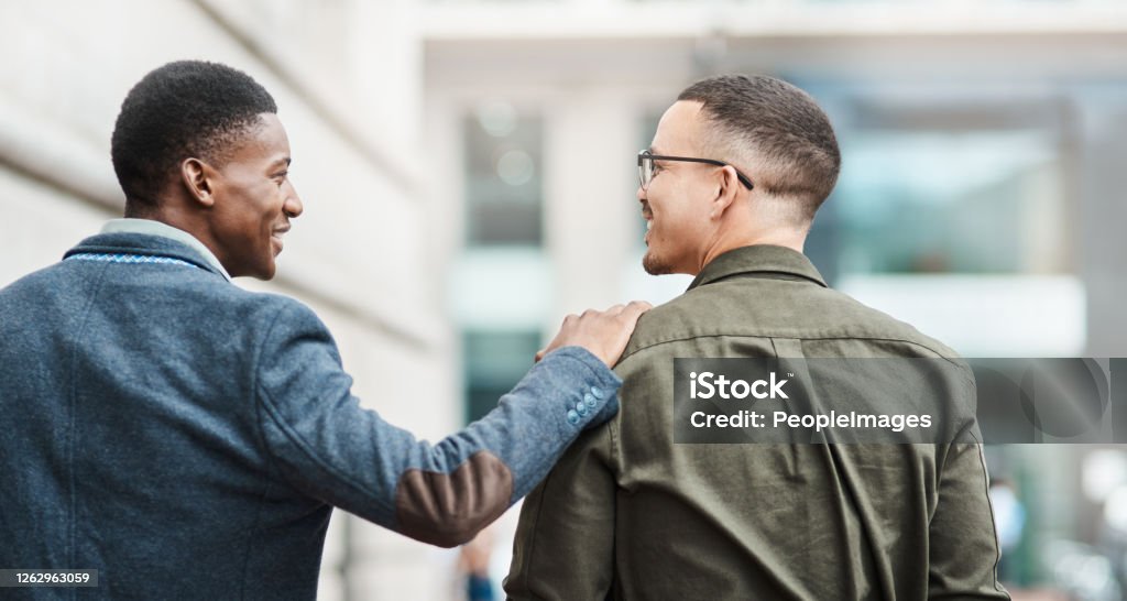 Who says you can’t be personal and professional? Rearview shot of two young businessmen walking through the city together Support Stock Photo