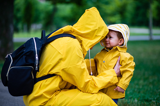 Mother and toddler child, boy, playing in the rain, wearing boots and raincoats