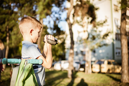 Young photographer with backpack and cap. Boy holding a digital camera and taking photos in the park.