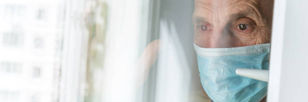 istock depressed pensioner in sterile face mask stands at window 1262968080