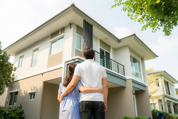 verticale arrière de jeune couple asiatique restant et étreignant ensemble regardant heureux devant leur nouvelle maison pour commencer une nouvelle vie. la famille, l’âge, la maison, l’immobilier et le concept de personnes. - bâtiment vu de photos et images de collection