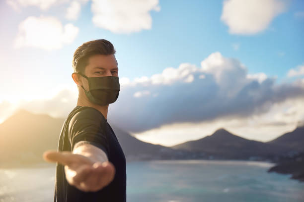 Man wearing face mask holding out his hand with scenic view.