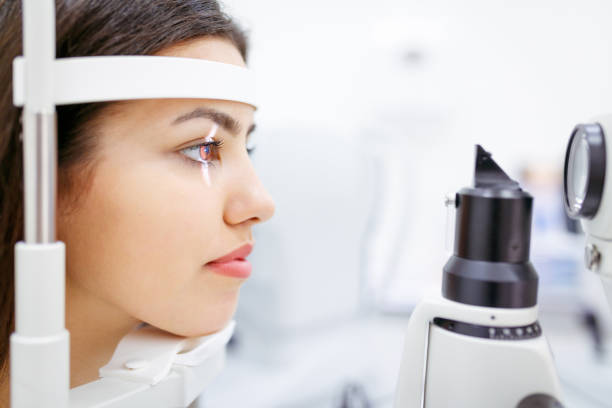 istock Female patient leaning head on optical instrument for eye exam 1262979554