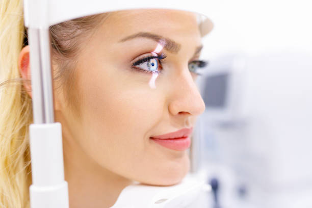 Beautiful young woman on eyesight check-up Beautiful young woman leaning with chin on ophthalmic refractor frame to check eyesight visual sense stock pictures, royalty-free photos & images