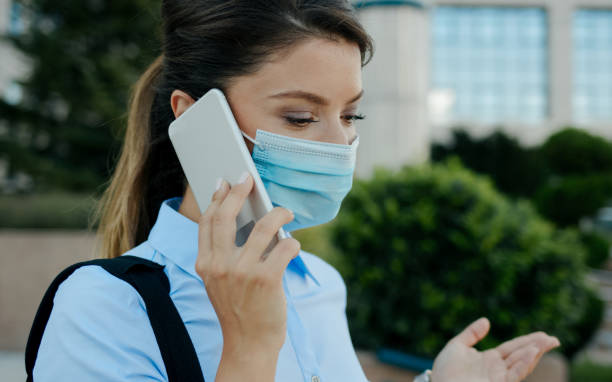 istock Businesswoman with protective face mask using smart phone outdoors 1262979849