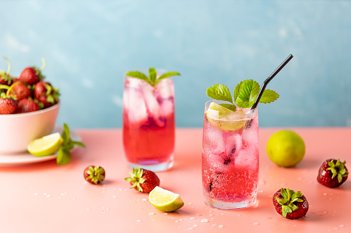 Two glasses with water drops of Strawberry mojito cocktail on light blue color background, pink board. Copy space, summer vacation and party concept