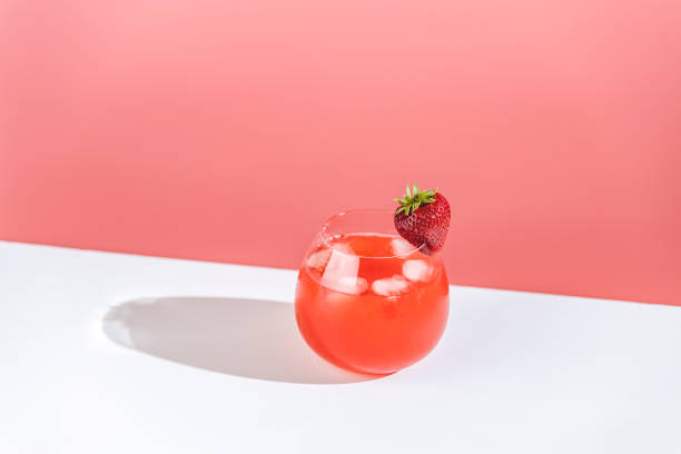 Strawberry mojito cocktail with ice in brandy glass with water drops on pastel soft pink color background in bright sun light, white board. Copy space, summer vacation and party concept stock photo