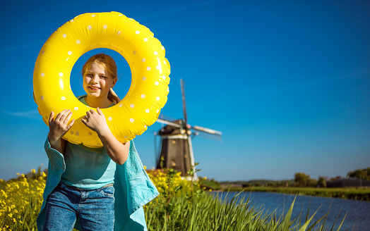 A  beautiful blonde Dutch school girl enjoying her free time at a typical dutch countryside windmill landscape on a beautiful sunny, blue sky day