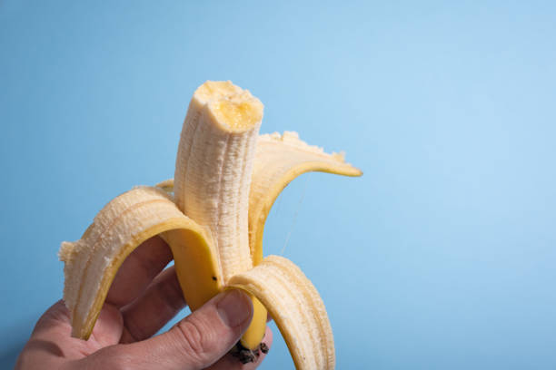 istock Hand holding bitten yellow banana and blue background 1262987365