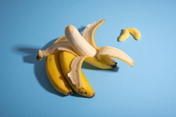 istock Open yellow banana sunbathing over blue desk against candy 1262987774