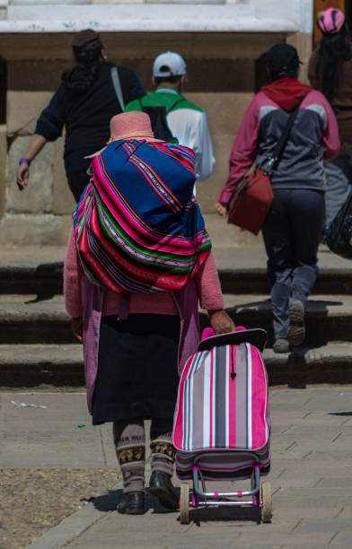 eine bolivianische frau trägt einen "aguayo" und einen einkaufssackwagen in copacabana, bolivien - bolivia copacabana bolivian ethnicity lake titicaca stock-fotos und bilder