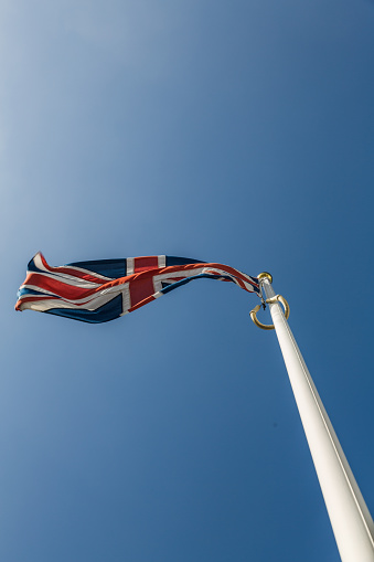 A union jack flagging flying in the breeze against a clear and bright blue summer sky