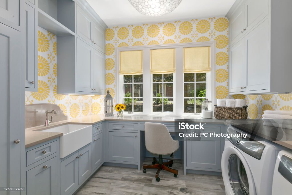 Farmhouse sink and desk add efficient options to this utility room Decorative wallpaper with gray cabinetry and new appliances Utility Room Stock Photo