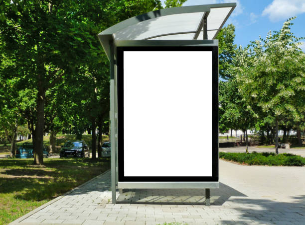 composite image of bus shelter at a bus stop. background for mock-up composite raster image of bus shelter at a bus stop of transparent clear glass and aluminum frame structure in green street setting with trees and street in the background. milky white poster ad and banner display glass. white light box. copy space. metaphoral stock pictures, royalty-free photos & images