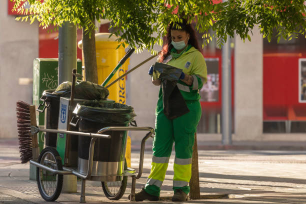 A worker in her daily cleaning tasks in Madrid Madrid, Spain - May 19, 2020: A worker in her daily cleaning tasks, in the morning, on the streets of Madrid, in the Retiro district. street sweeper stock pictures, royalty-free photos & images
