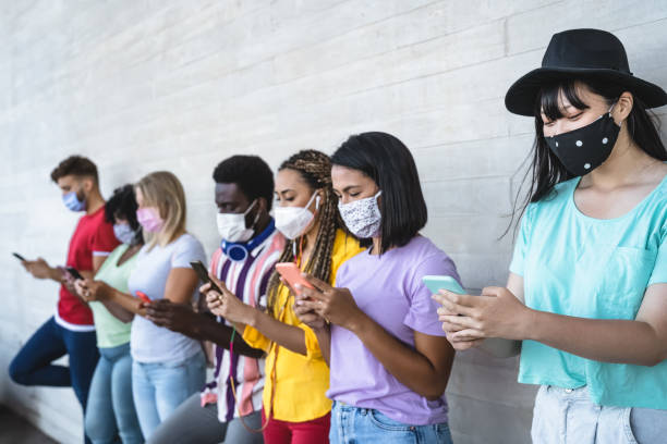 istock Young people wearing face mask using mobile smartphone outdoor - Multiracial friends having fun with new technology social media app during corona virus outbreak - Youth millennial lifestyle concept 1263008154