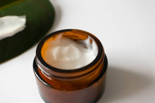istock Close-up open cream in brown glass jar and tropical leaf on background on white, selective focus. Moisturizer butter for skin care. Zero-waste eco-friendly packaging 1263010610