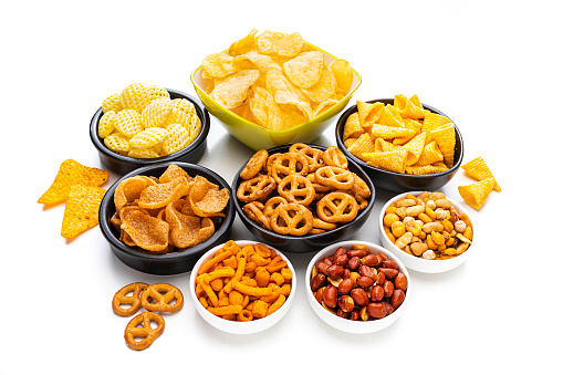 Party food: assortment of salty snacks in bowls shot on white background. High angle view. Predominant colors are yellow and white. High resolution 42Mp studio digital capture taken with SONY A7rII and Zeiss Batis 40mm F2.0 CF lens