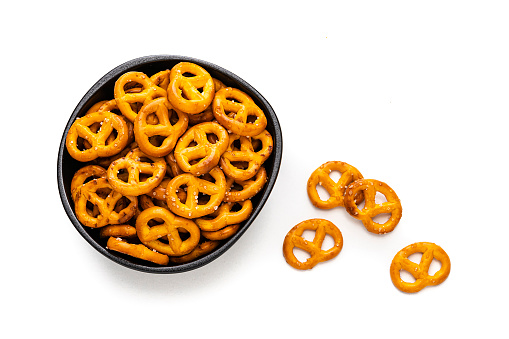 Party food: snack pretzels in a black bowl shot from above on white background. Predominant colors are gold and white. High resolution 42Mp studio digital capture taken with SONY A7rII and Zeiss Batis 40mm F2.0 CF lens