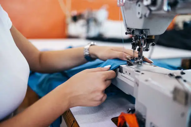 Close up shot of professional seamstress hands working in tailoring or sewing industry production hall.