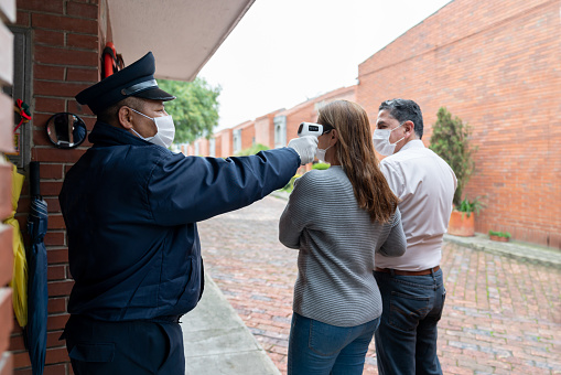 Security guard checking the temperature of a couple at the gate of their neighborhood using an infrared thermometer -COVID-19 pandemic lifestyle