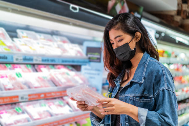 식료품점에서 얼굴 마스크를 쓰고 있는 젊은 아시아 여성 - supermarket meat women packaging 뉴스 사진 이미지