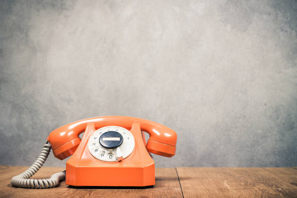 istock Old orange retro rotary telephone from 60s on table front textured concrete wall background. Vintage style filtered photo 1263027914