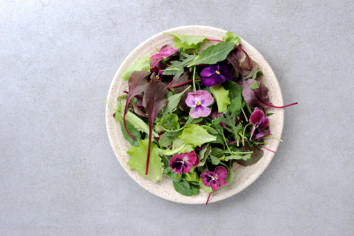 Fresh salad with edible flowers in the plate over background.Flat lay,horizontal.
