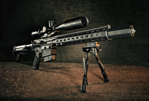 Dramatic studio shot of a rifle on a bipod with a silencer and an optic, ready to fire!