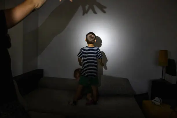 Photo of Mother playing with kids and making shadow puppets on wall