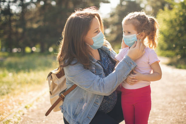 Mother and daughter walking outdoors with protective face masks stock photo