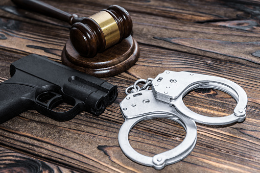 handcuffs, a judge hammer, a gun on a wooden background. criminal offense