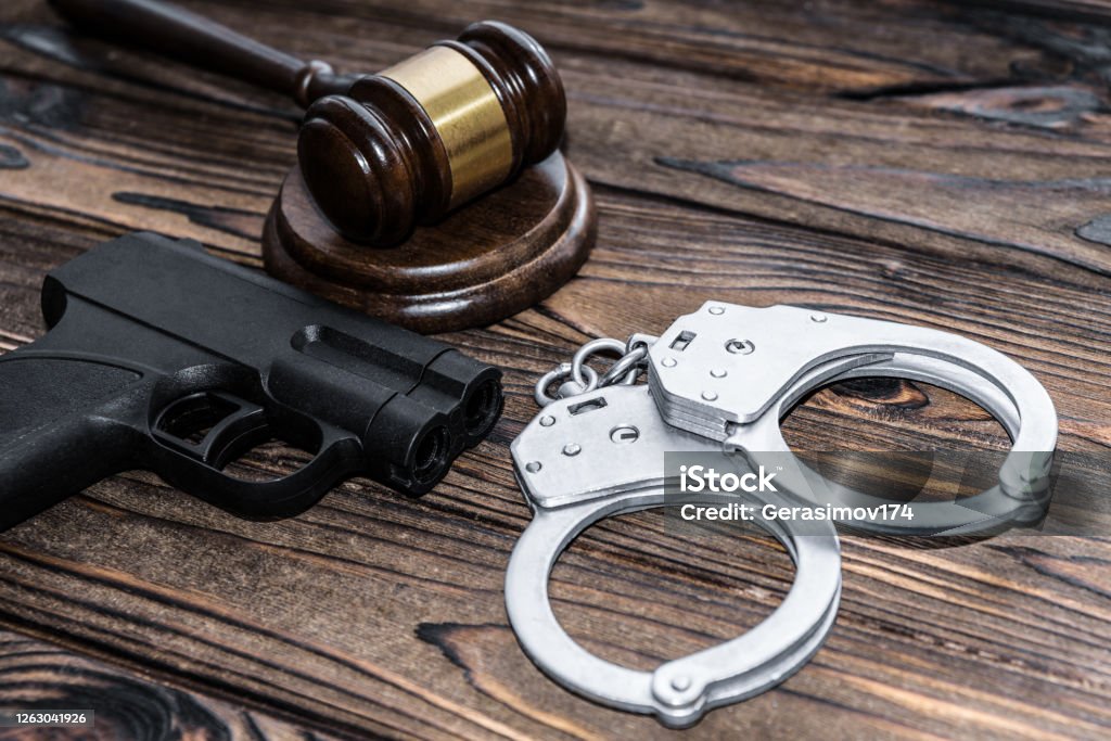 handcuffs, a judge hammer, a gun on a wooden background. criminal offense Weapon Stock Photo