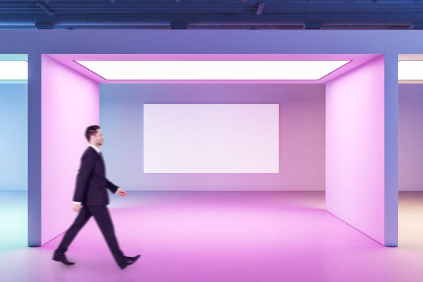 istock Businessman walking in gallery interior with blank poster on wall. 1263043568